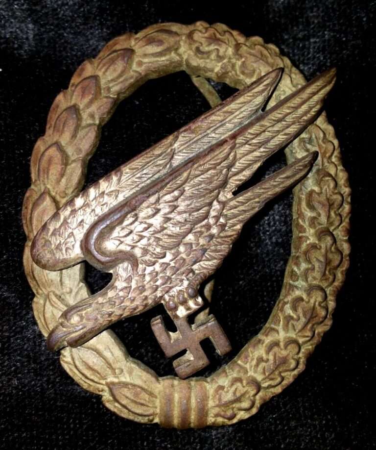 Distintivo ovale in metallo brunito: una corona di foglie con un'aquila in picchiata che stringe una svastica, su velluto nero.