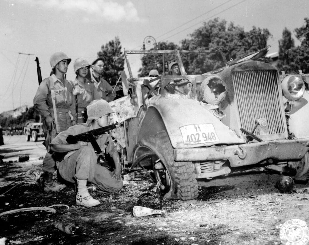 Fotografia in bianco e nero: soldati americani con l'elmetto osservano un veicolo militare tedesco distrutto in una strada di Livorno.