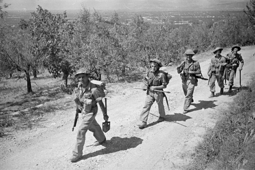 Fila di soldati neozelandesi con elmetto e fucile che cammina lungo una strada di campagna verso Firenze.