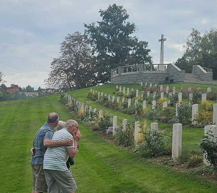 Un uomo anziano e il figlio si abbracciano fra le lapidi del cimitero di guerra sudafricano di Castiglione dei Pepoli