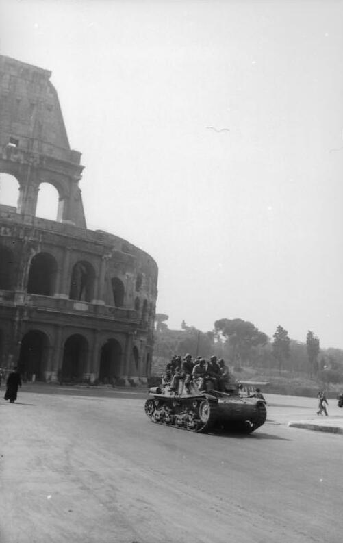Il Colosseo sullo sfondo; davanti, su una strada deserta, un piccolo carro armato con alcuni soldati a bordo.